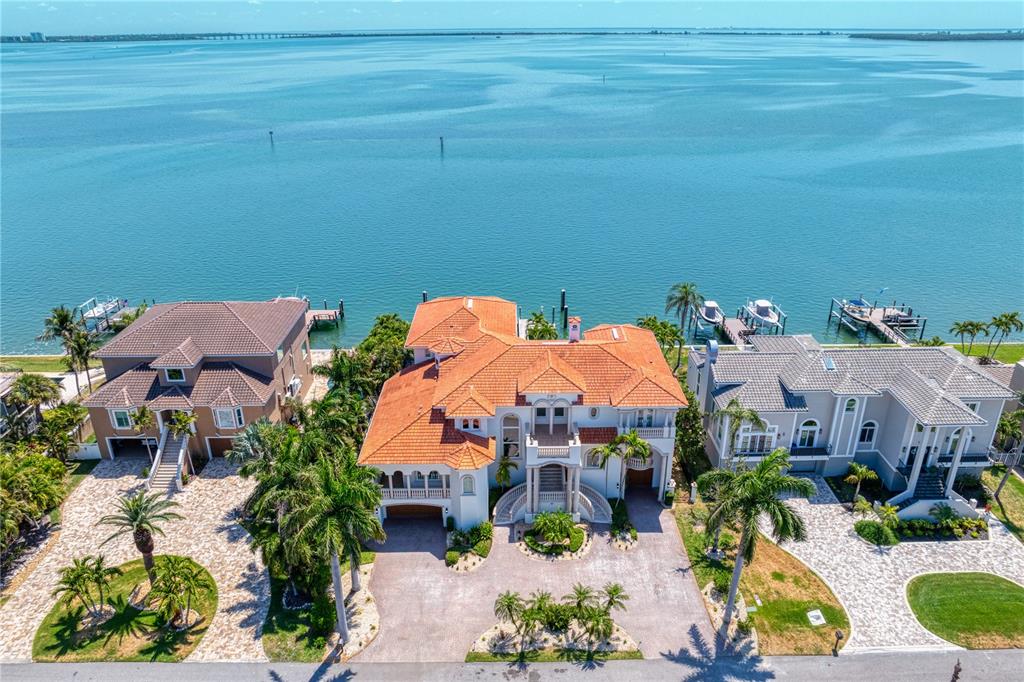 An aerial view shows three waterfront houses with tiled roofs and private docks on the bay — 611 1ST AVENUE S, TIERRA VERDE, FL