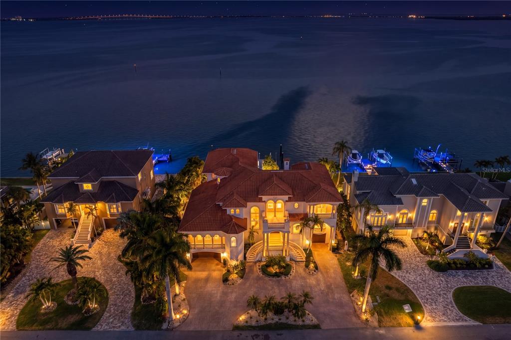 An aerial night view of three waterfront houses with illuminated exteriors and private boat docks — 611 1ST AVENUE S, TIERRA VERDE, FL
