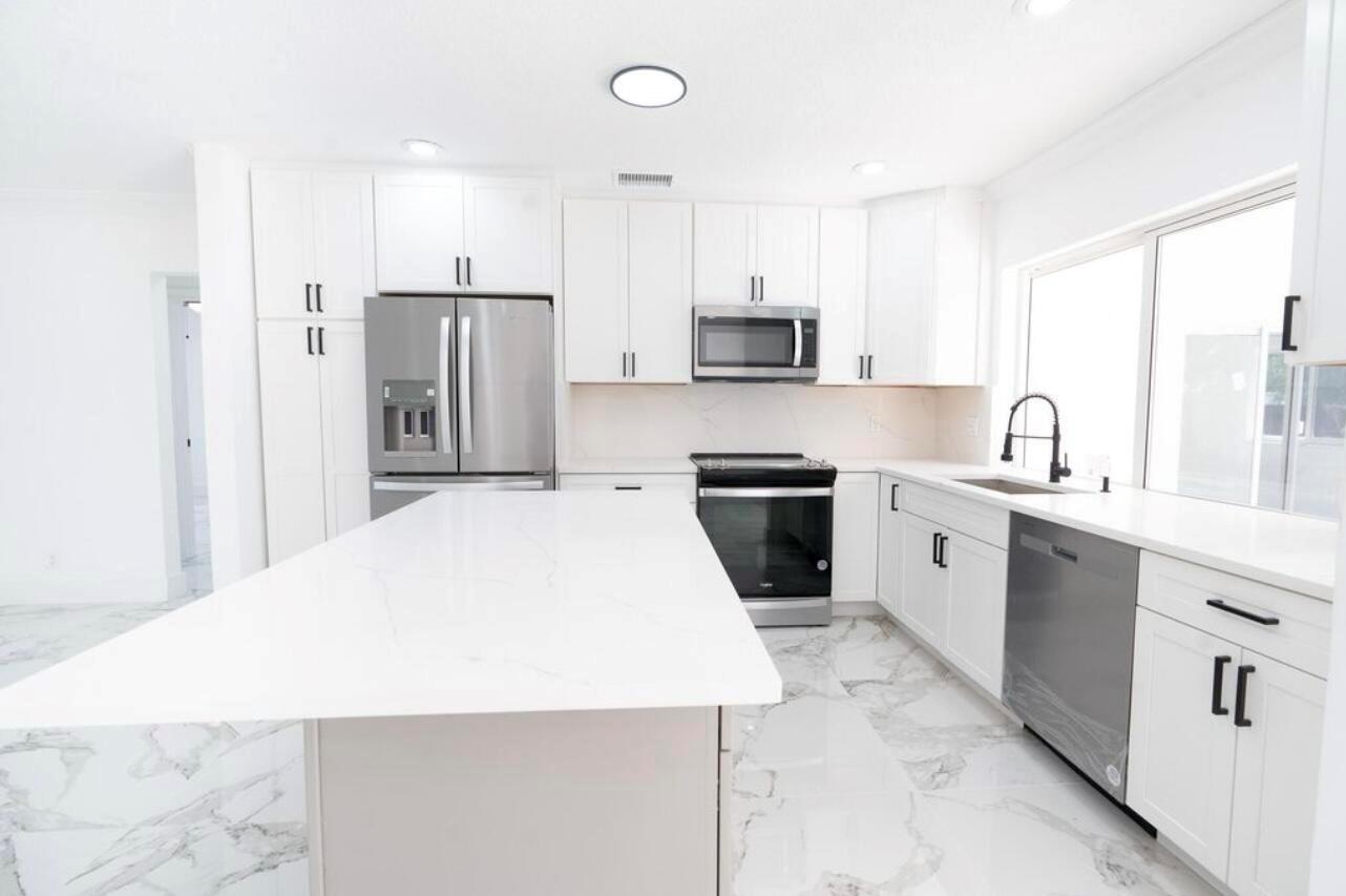 A modern white kitchen features a large island, stainless steel appliances, and marble-patterned tile flooring — 1070 SW 18th Street, Boca Raton FL 33486, BOCA RATON, FL