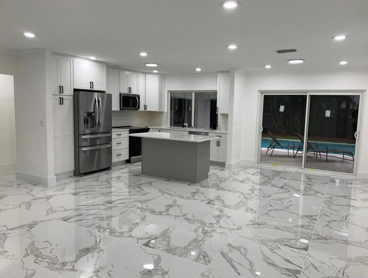 A modern kitchen features white cabinetry, a gray island, and polished marble-look tile flooring — 1070 SW 18th Street, Boca Raton FL 33486, BOCA RATON, FL