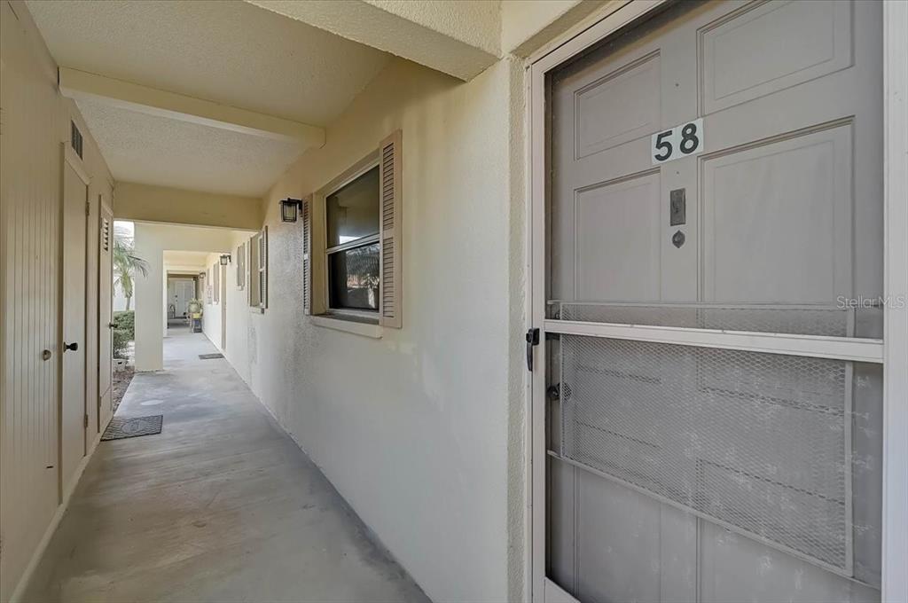 A covered outdoor walkway leads to a gray front door marked with the number 58 — 2875 SWIFTON DRIVE UNIT 58, SARASOTA, FL