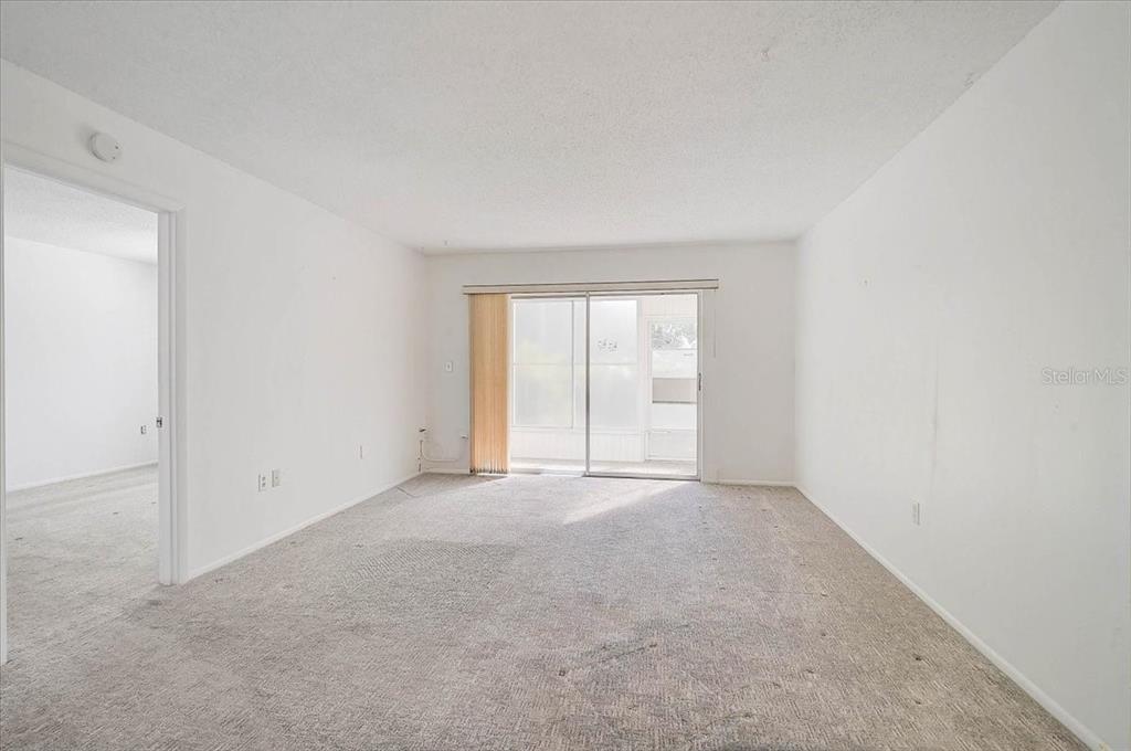 An empty living room features white walls, beige carpeting, and a sliding glass door — 2875 SWIFTON DRIVE UNIT 58, SARASOTA, FL