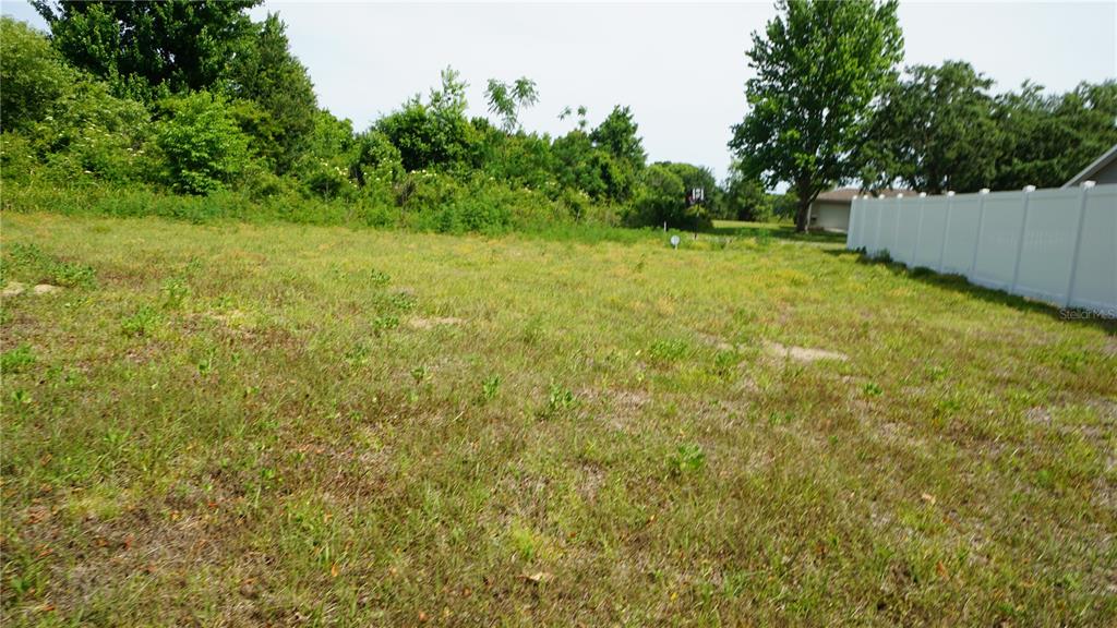 A grassy, vacant lot is bordered by a white vinyl fence and dense trees — MARILYN AVENUE, HOWEY IN THE HILLS, FL
