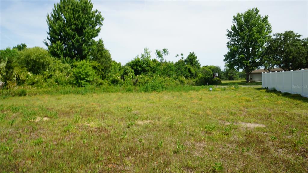 A vacant, grassy residential lot features dense trees in the background and a white fence — MARILYN AVENUE, HOWEY IN THE HILLS, FL
