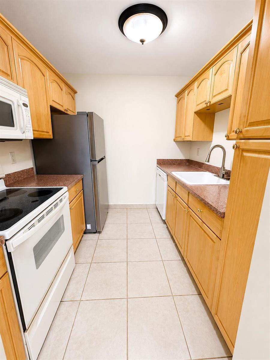 A galley kitchen features light wood cabinets, granite countertops, and stainless steel appliances — 1918 Palmland Drive # 2, Boynton Beach FL 33436, BOYNTON BEACH, FL