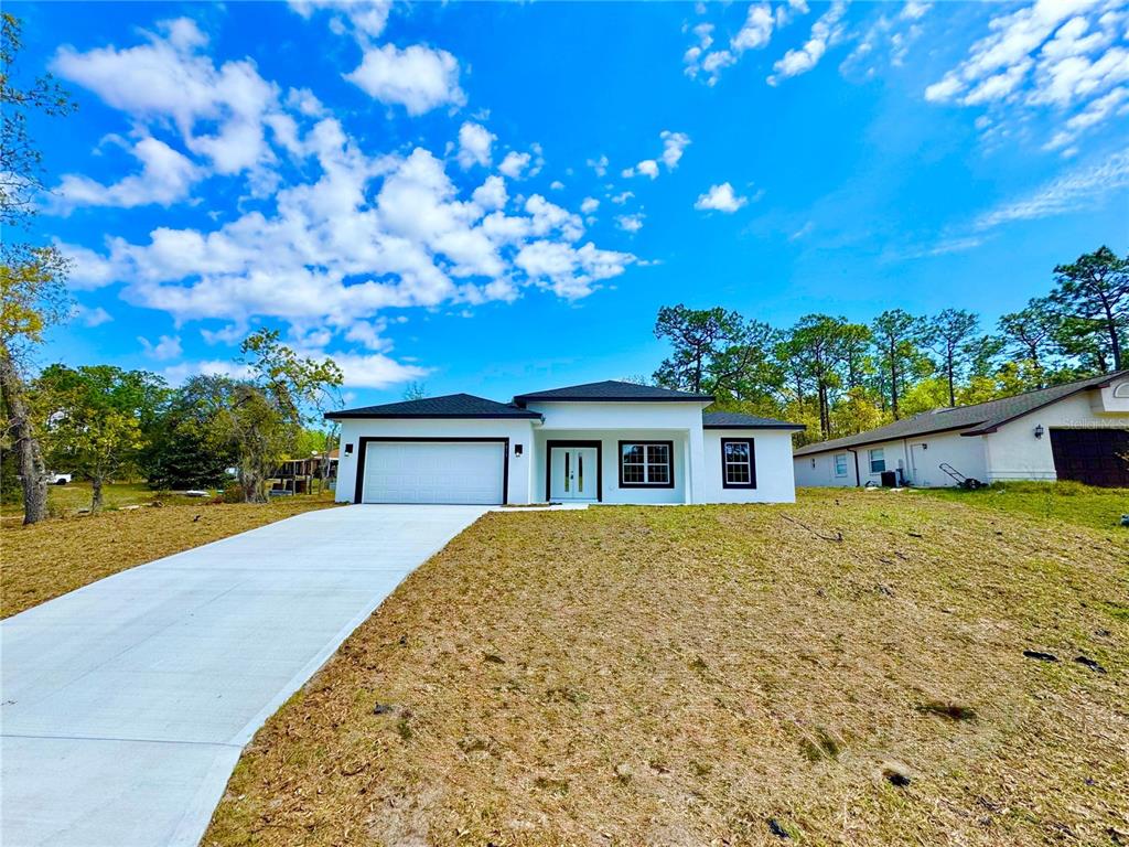 A modern, single-story white house with a two-car garage and a concrete driveway — 7815 N PRIMROSE DRIVE, CITRUS SPRINGS, FL