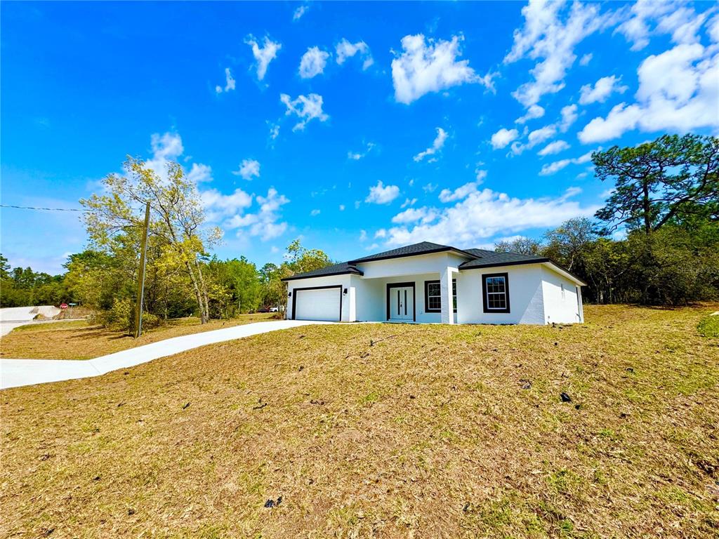 A white single-story house with a black roof and garage sits on a grassy lot — 7815 N PRIMROSE DRIVE, CITRUS SPRINGS, FL
