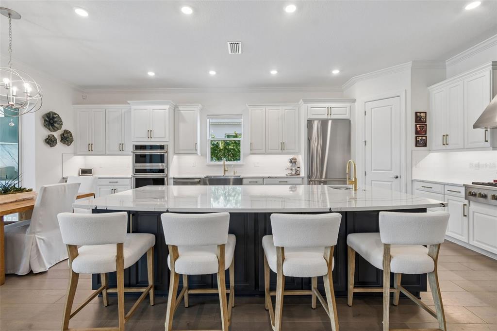 A modern kitchen features white cabinetry, a dark island with seating, and stainless steel appliances — 15424 SAN LAZZARO AVENUE, BRADENTON, FL