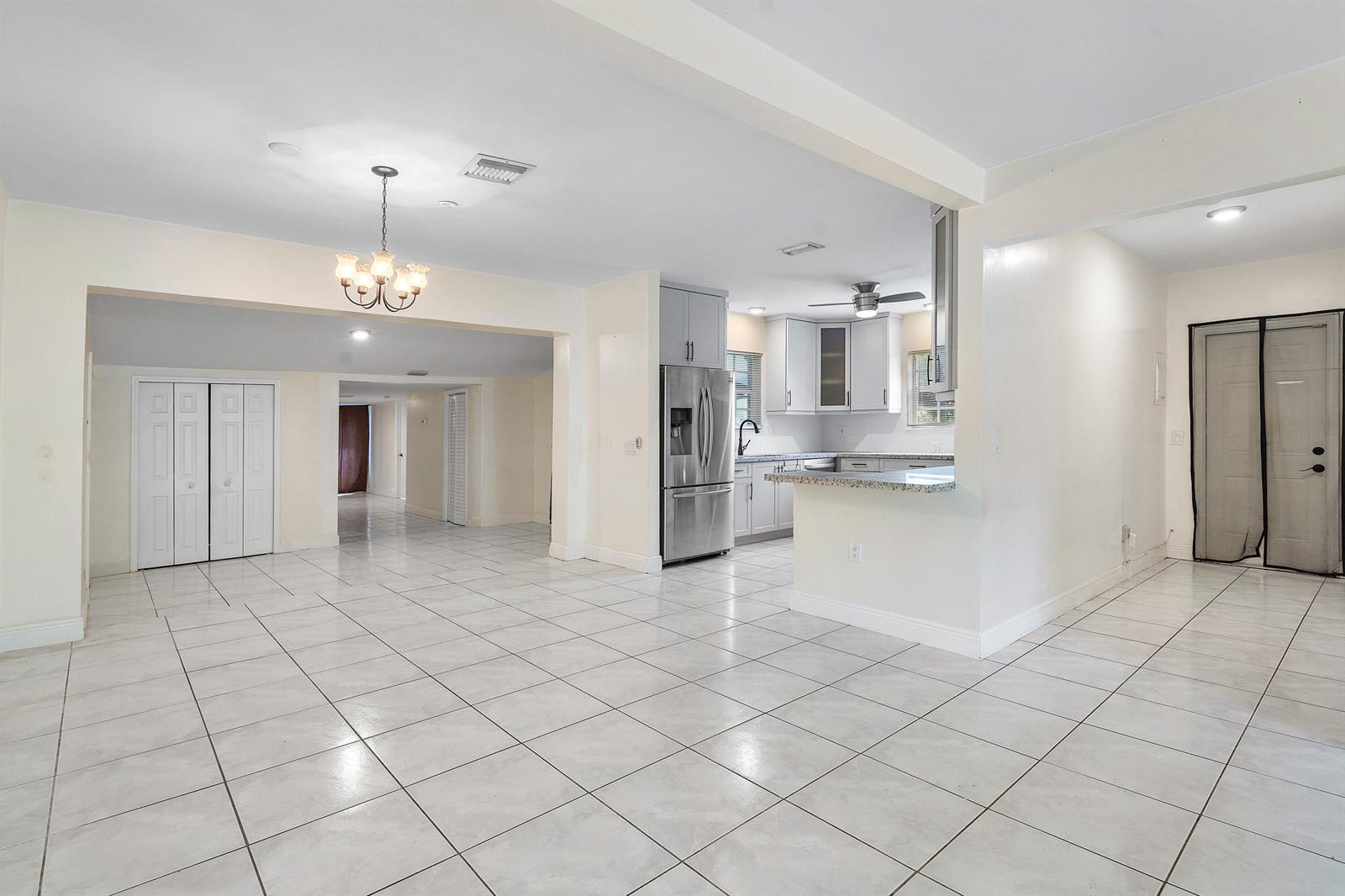 An open-concept living area features white tile flooring, a kitchen with stainless appliances, and a chandelier — 6130 Edwards Road, Margate FL 33063, MARGATE, FL