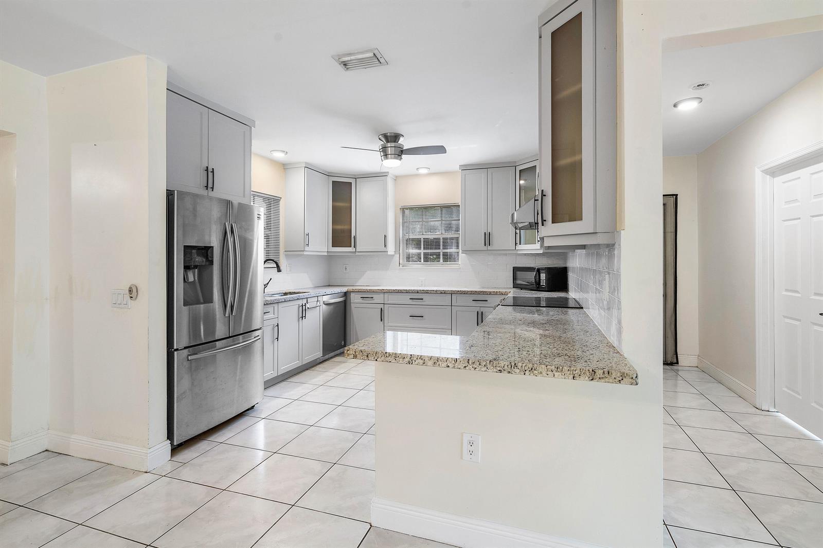A kitchen features gray cabinets, stainless steel appliances, granite countertops, and light tile flooring — 6130 Edwards Road, Margate FL 33063, MARGATE, FL