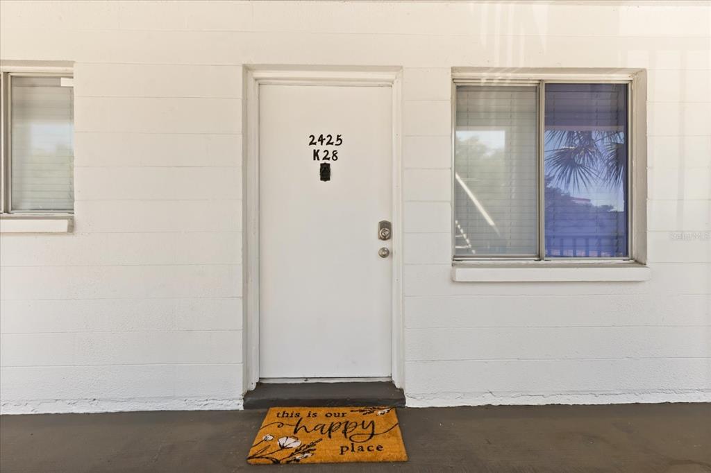 A white exterior door with a welcome mat sits between two windows on a building — 2425 FLAMINGO BOULEVARD UNIT K28, BRADENTON, FL