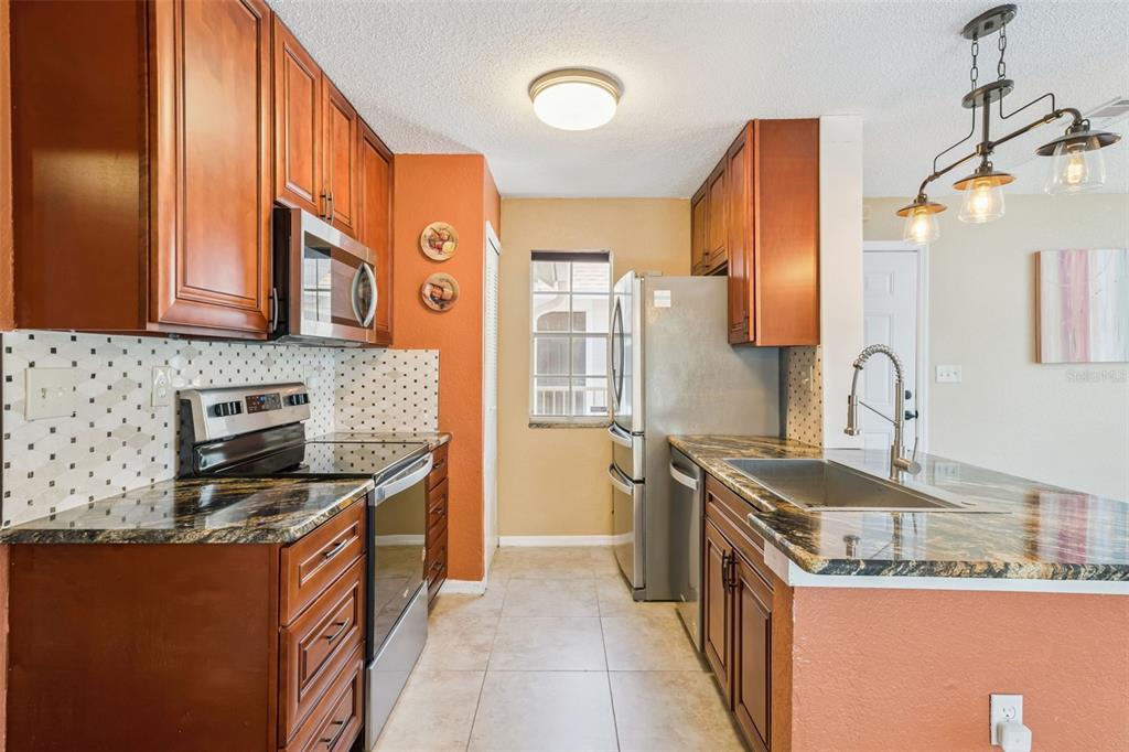 A kitchen with wood cabinets, granite countertops, stainless steel appliances, and a tile backsplash — 634 STEAMBOAT COURT UNIT 172, ALTAMONTE SPRINGS, FL