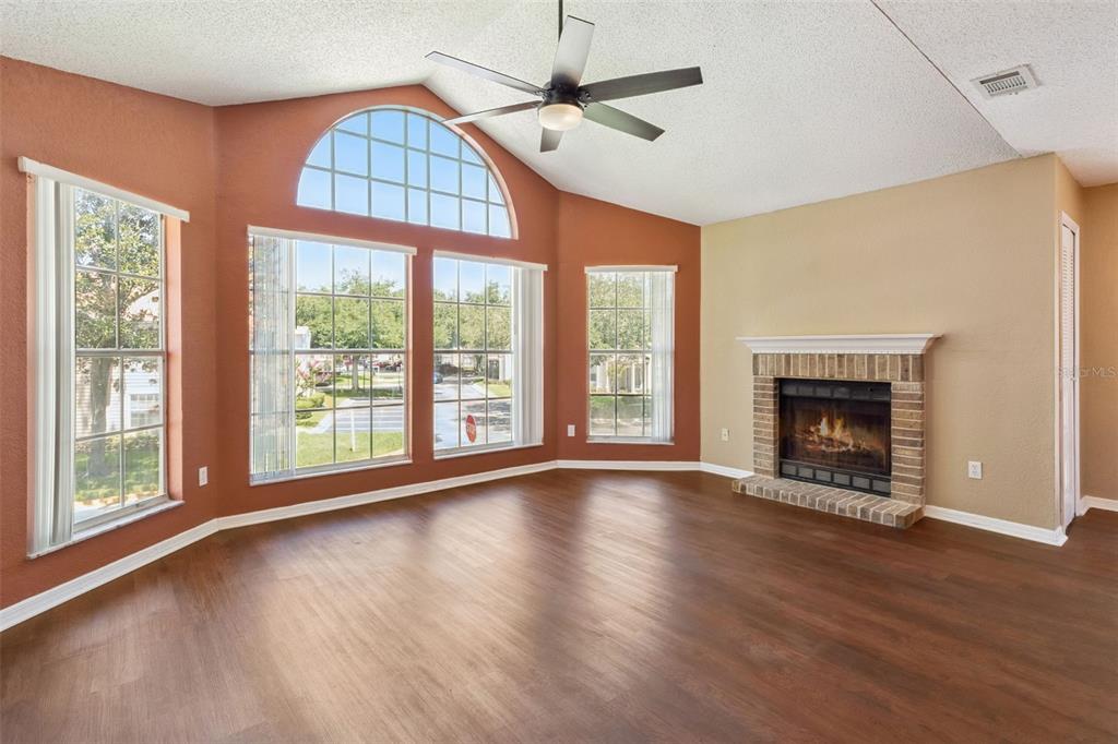 A living room with wood-look flooring, a brick fireplace, and large windows with an arch — 634 STEAMBOAT COURT UNIT 172, ALTAMONTE SPRINGS, FL