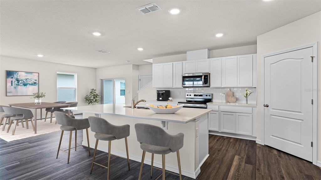 A modern kitchen features white cabinets, a large island with bar stools, and dark flooring — 5174 BLANKET FLOWER STREET, APOPKA, FL