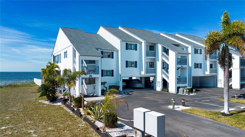 A multi-story white building with blue shutters sits near the ocean with a parking area — 802 BAHIA DEL SOL DRIVE UNIT 6, RUSKIN, FL