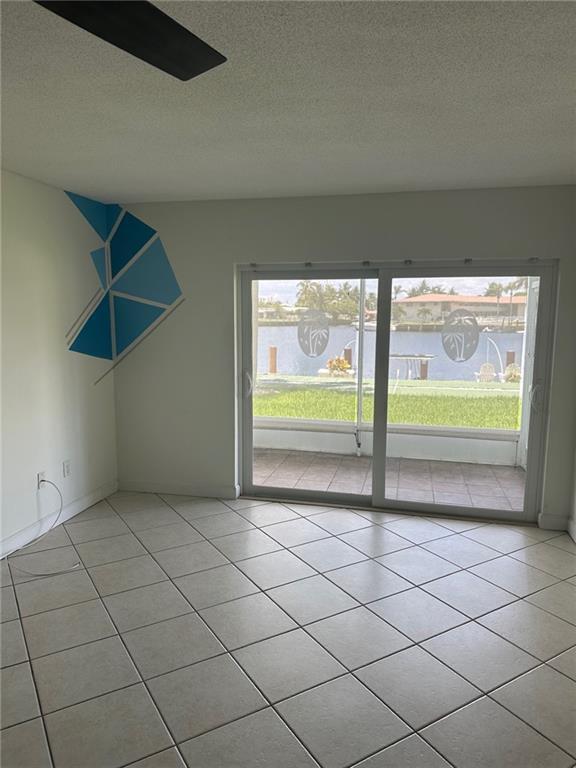 A room with tiled floors and a sliding glass door overlooking a canal and lawn — 750 Pine Drive # 2, Pompano Beach FL 33060, POMPANO BEACH, FL
