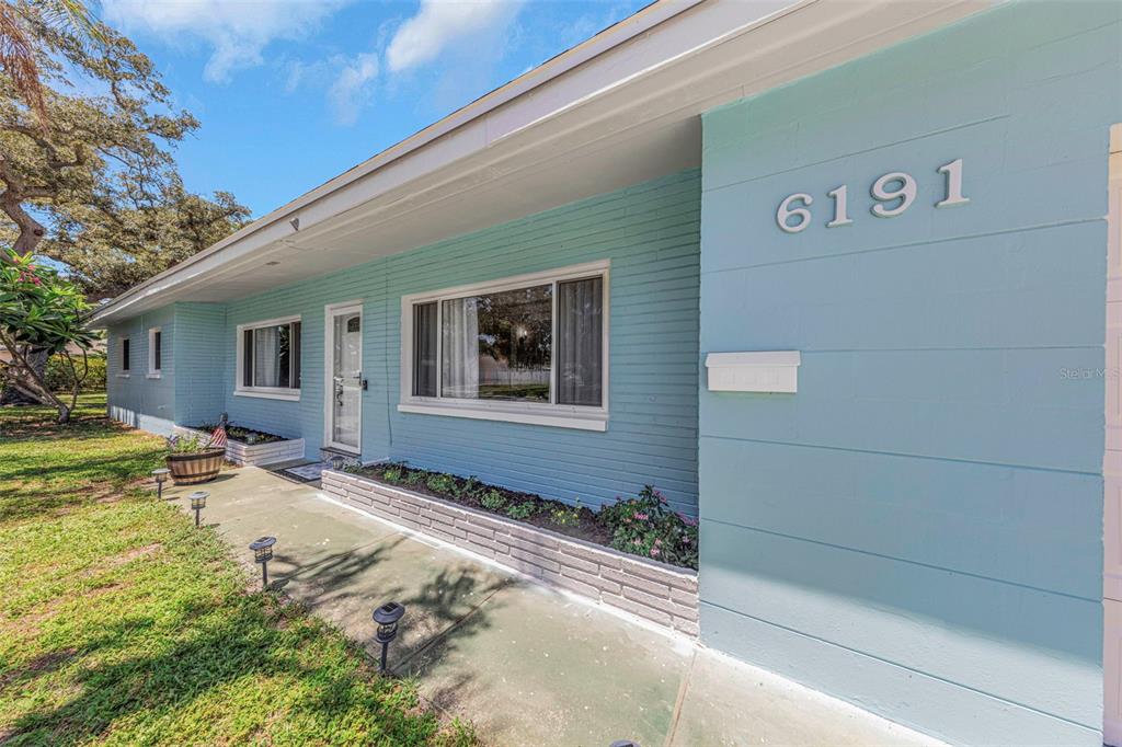 A light blue painted brick house exterior features a front walkway and a small garden bed — 6191 6TH AVENUE S, ST PETERSBURG, FL