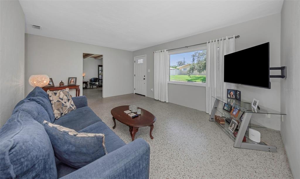 A living room features a blue sofa, a glass TV stand, and speckled flooring — 6191 6TH AVENUE S, ST PETERSBURG, FL
