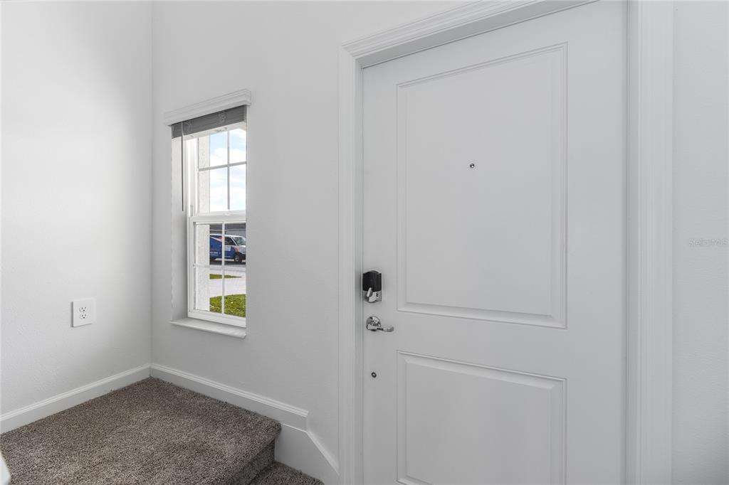 A white door with a smart lock sits next to a window above carpeted stairs — 2363 BURNEY FALLS LN LANE, DAVENPORT, FL