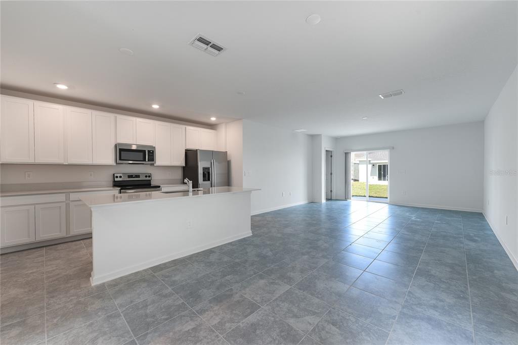 A kitchen with white cabinets and a center island opens to a tiled living area — 2363 BURNEY FALLS LN LANE, DAVENPORT, FL
