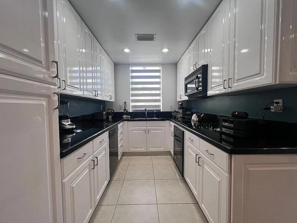 A galley kitchen features white cabinets, black countertops, and light-colored tile flooring — 6463 La Costa Drive # 105, Boca Raton FL 33433, BOCA RATON, FL