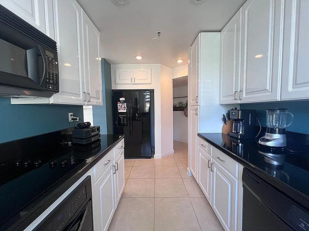 A galley kitchen features white cabinets, black countertops, stainless steel appliances, and teal accent walls — 6463 La Costa Drive # 105, Boca Raton FL 33433, BOCA RATON, FL