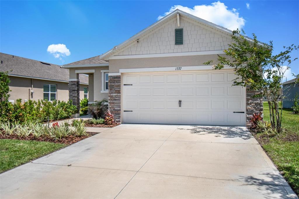 A single-story house with a white garage door, stone accents, and a concrete driveway — 1337 CORK DRIVE, ORMOND BEACH, FL