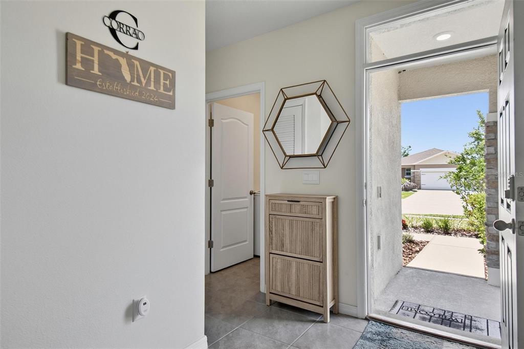 An entryway features a light wood shoe cabinet, a hexagonal mirror, and a front door — 1337 CORK DRIVE, ORMOND BEACH, FL