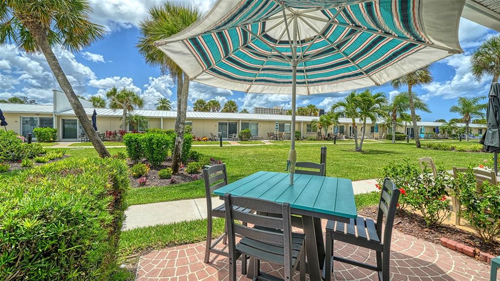 A patio with a table, chairs, and umbrella overlooks a grassy courtyard with palm trees — 5830 MIDNIGHT PASS ROAD UNIT 32, SARASOTA, FL
