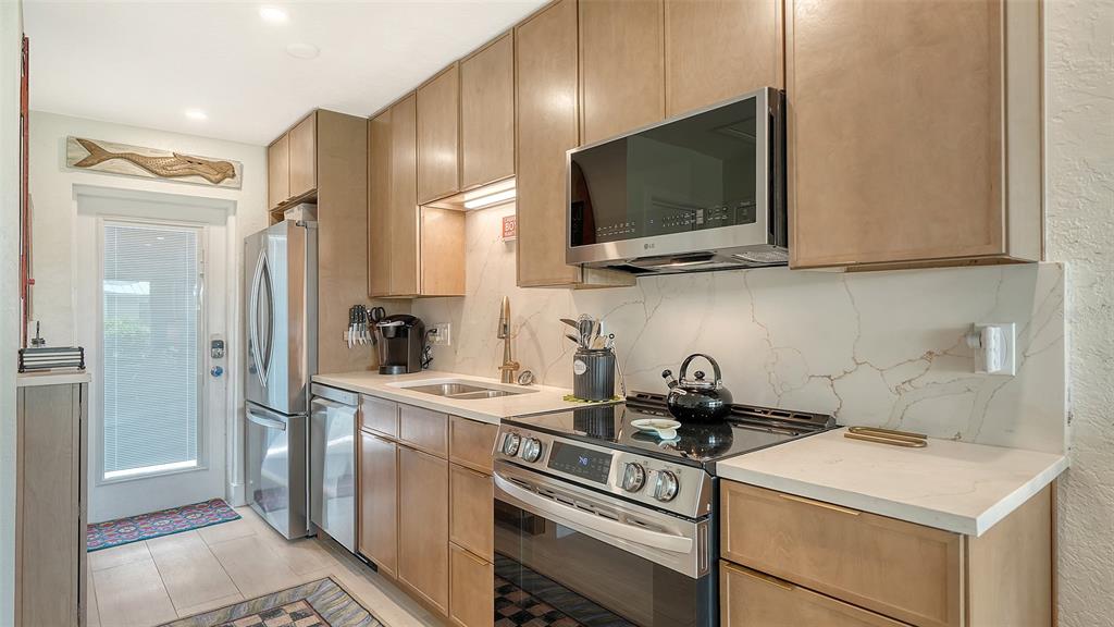 A galley kitchen features light wood cabinets, stainless steel appliances, and a white marble backsplash — 5830 MIDNIGHT PASS ROAD UNIT 32, SARASOTA, FL