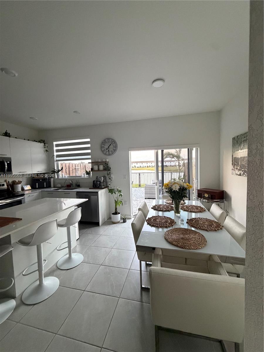 An open-concept kitchen and dining area features white cabinetry, a breakfast bar, and sliding doors — 2371 NW 122nd Ter, Miami FL 33167, MIAMI, FL