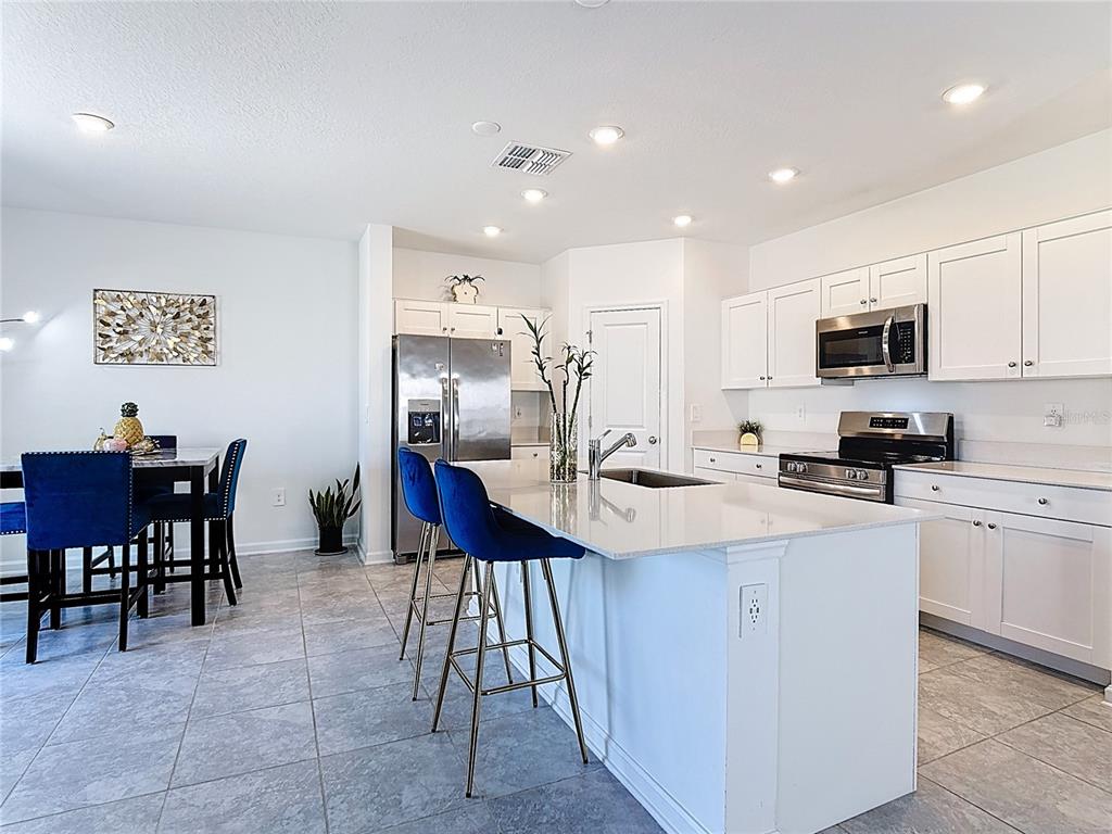A kitchen features white cabinets, a central island with bar seating, and stainless steel appliances — 629 SAND PINE LANE, HAINES CITY, FL