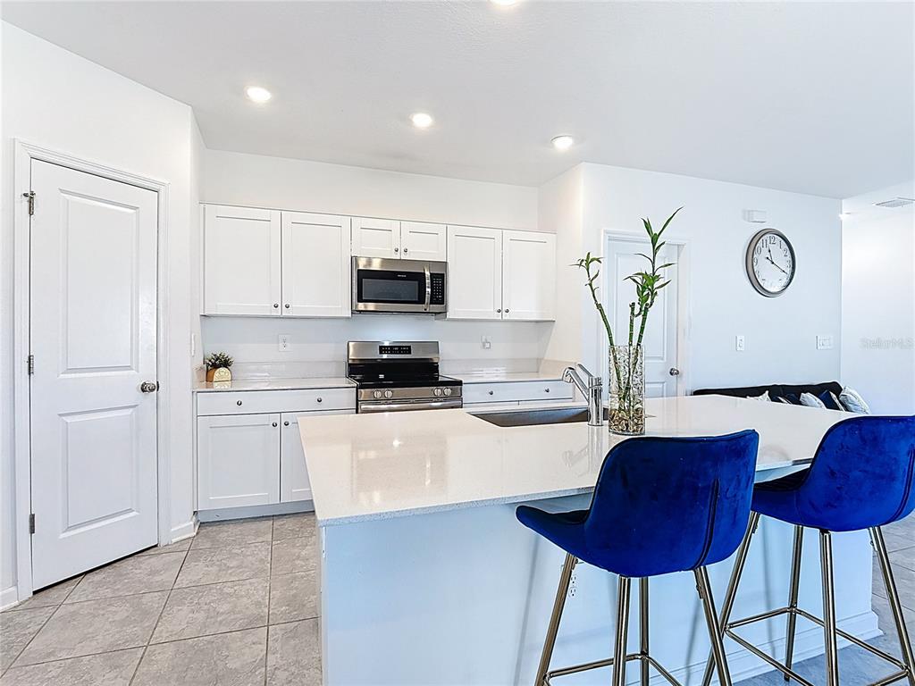 A kitchen features white cabinets, stainless steel appliances, a quartz island, and blue bar stools — 629 SAND PINE LANE, HAINES CITY, FL