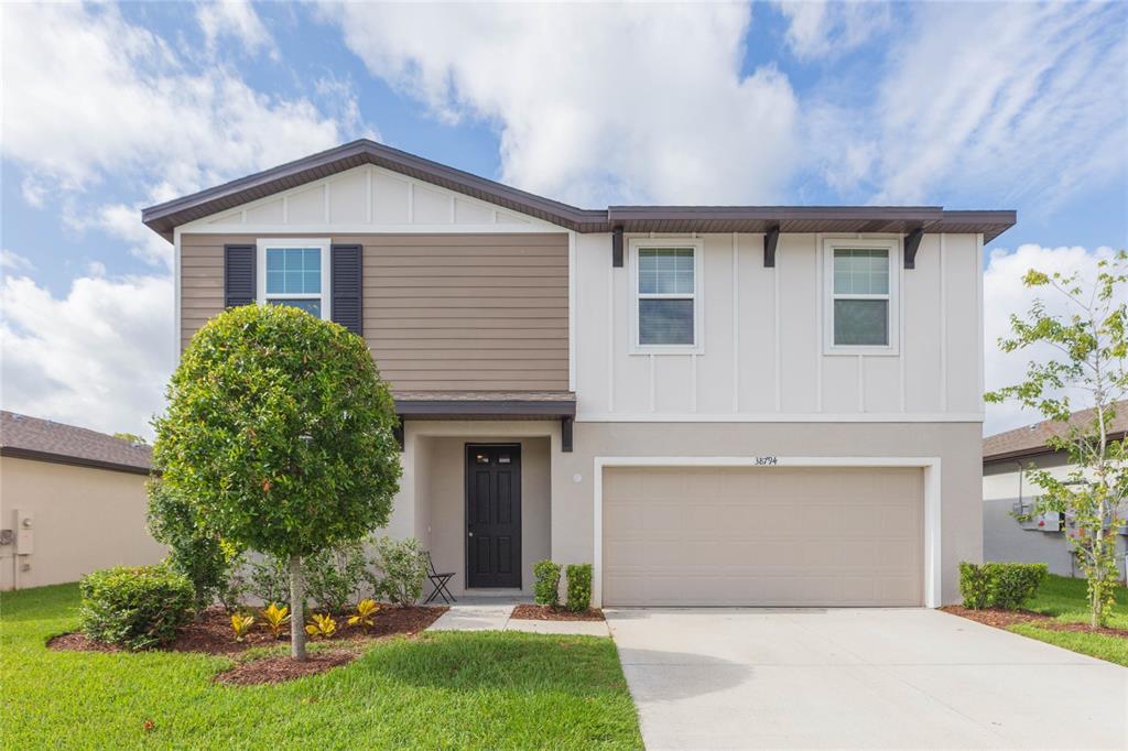 A two-story house with a tan garage, brown siding, and a white facade — 38794 OPAL WILLOW LANE, ZEPHYRHILLS, FL