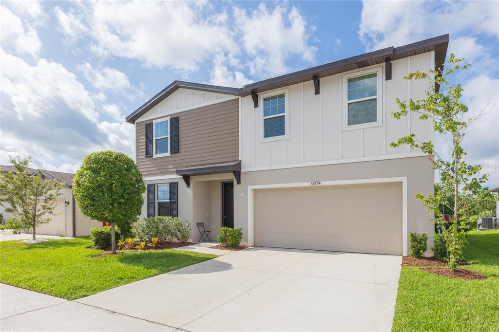 A two-story house with a beige garage, brown siding, and white vertical paneling — 38794 OPAL WILLOW LANE, ZEPHYRHILLS, FL