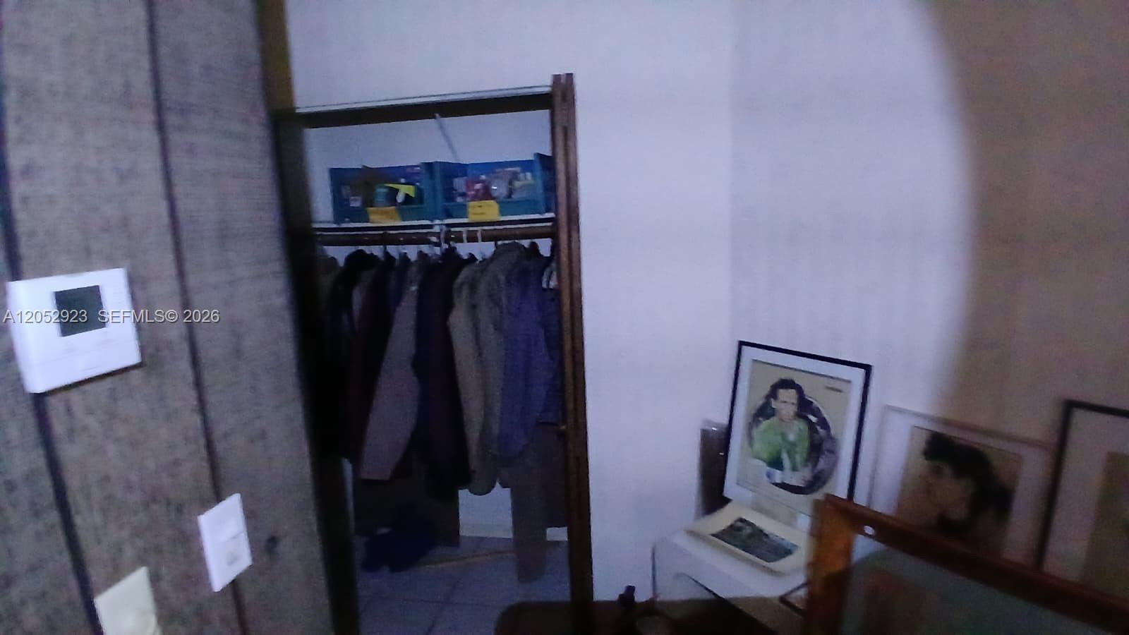 A closet with hanging clothes sits next to framed pictures on a white wall — CORAL SPRINGS, FL