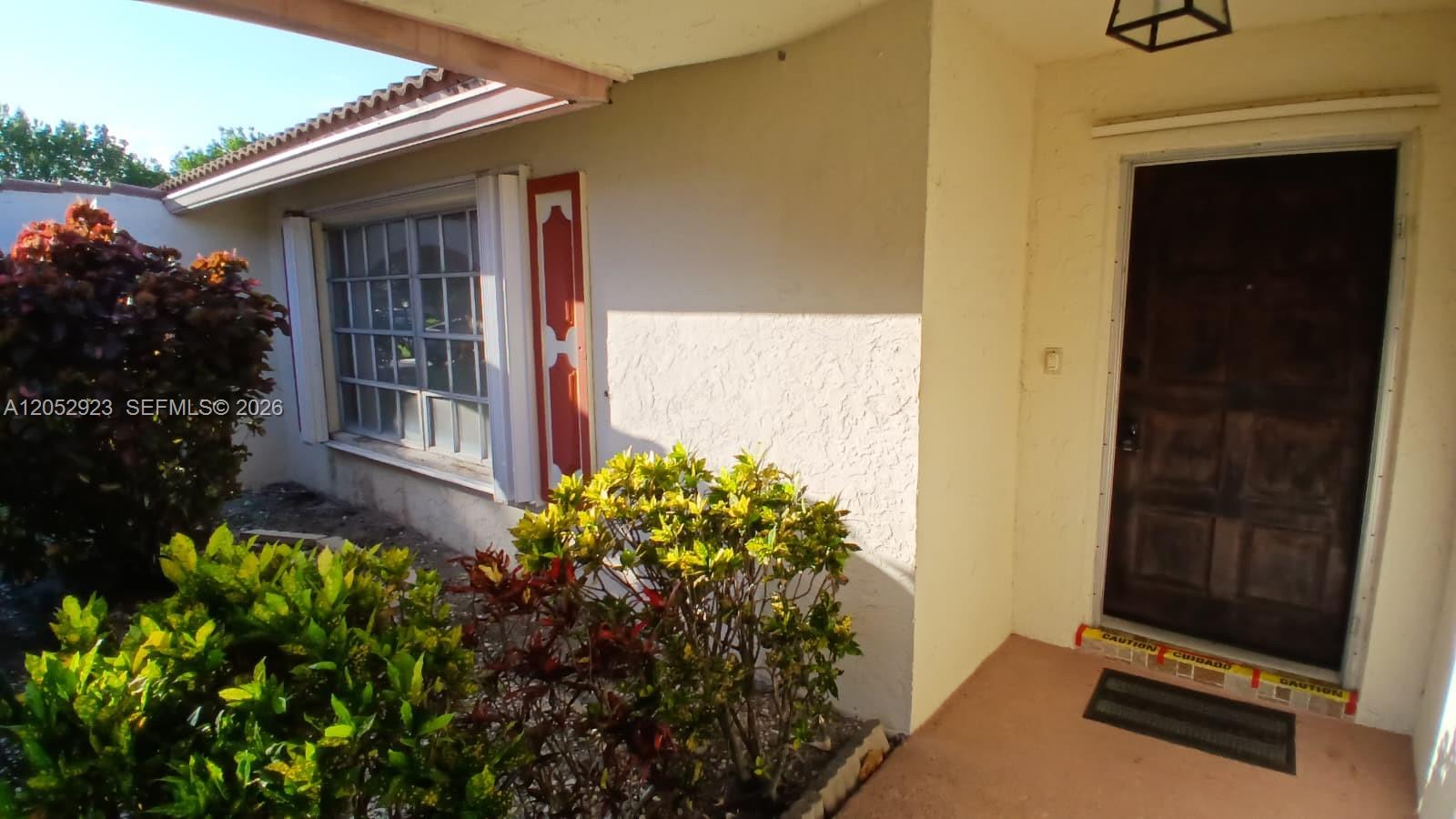 The exterior of a house features a front door, a window with red shutters, and landscaping — CORAL SPRINGS, FL