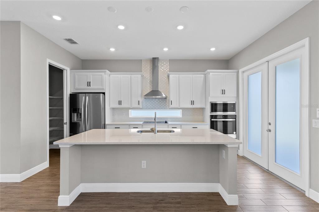 A modern kitchen features white cabinets, a large quartz island, and stainless steel appliances — 10205 PEARSON AVENUE, ORLANDO, FL