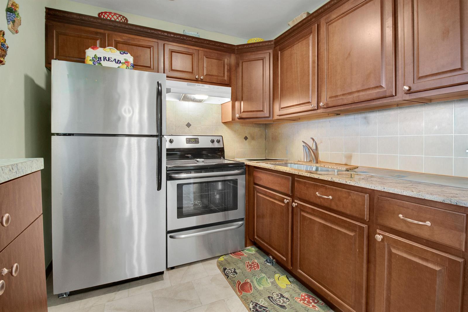 A kitchen features wood cabinets, stainless steel appliances, and a tiled backsplash — 412 Brighton J, Boca Raton FL 33434, BOCA RATON, FL