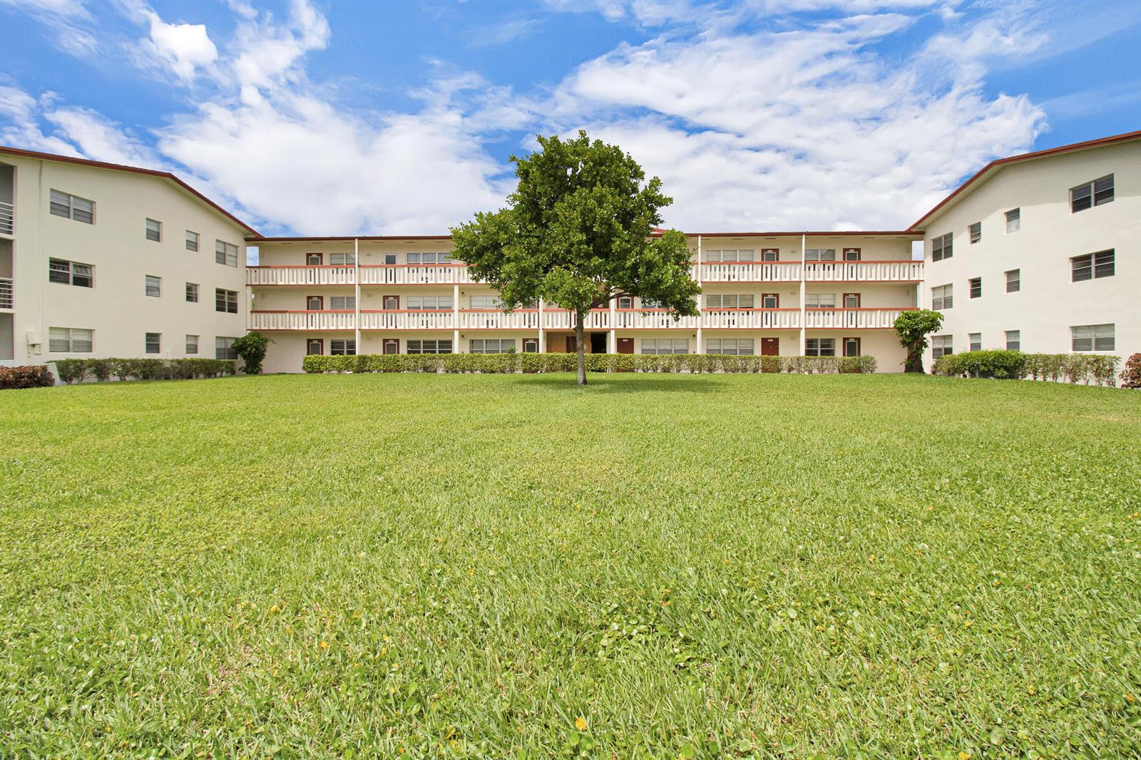 A three-story apartment building with a central courtyard and a large tree on the lawn — 412 Brighton J, Boca Raton FL 33434, BOCA RATON, FL