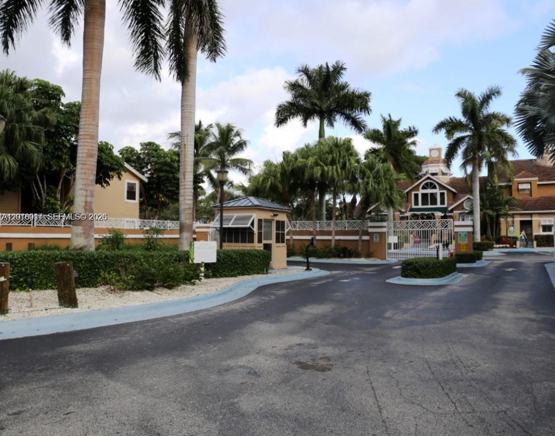 A gated entrance with a guardhouse, palm trees, and a white fence under a blue sky — 15640 SW 106th Ln # 903, Miami FL 33196, MIAMI, FL