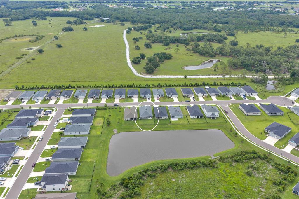 An aerial view shows a residential neighborhood with houses bordering a pond and green fields — 6543 166TH PLACE E, PARRISH, FL
