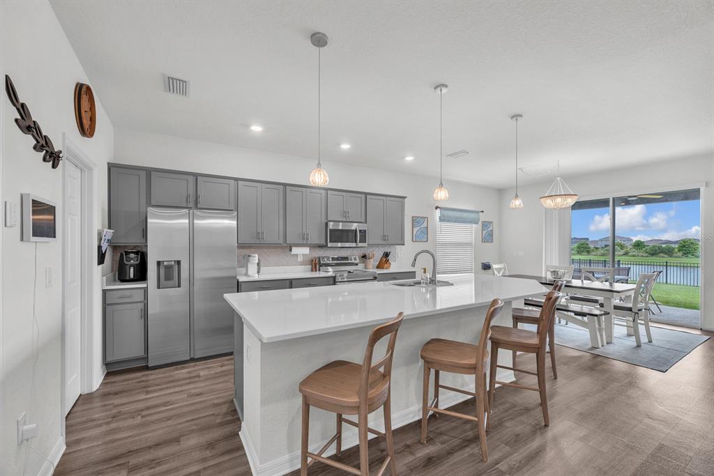 A kitchen features gray cabinets, a white quartz island, and a dining area with patio access — 6543 166TH PLACE E, PARRISH, FL