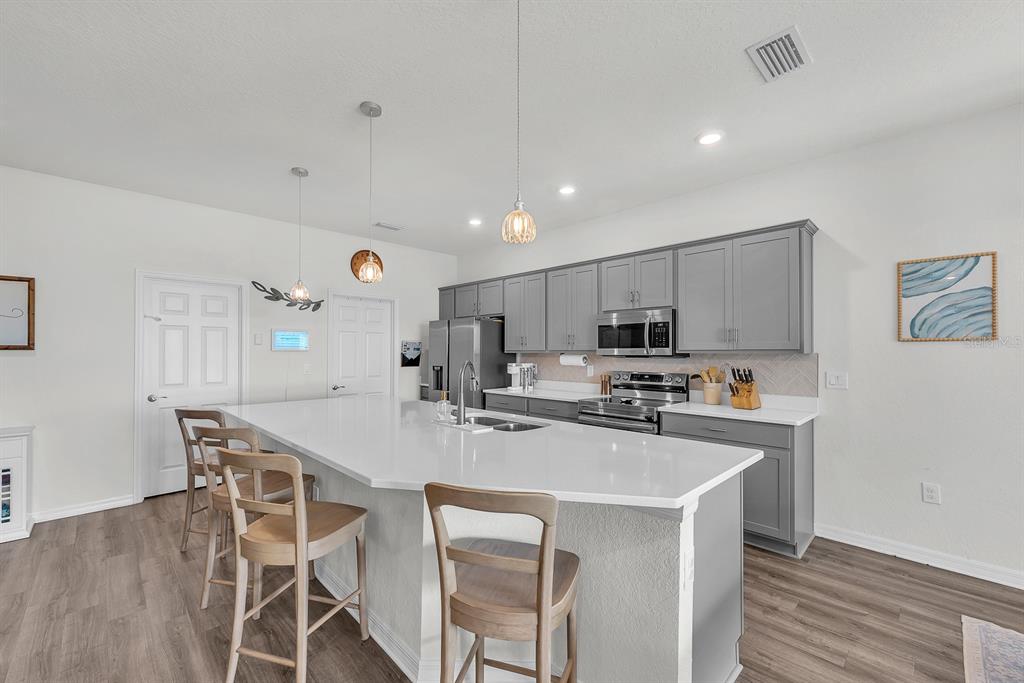 A kitchen features a large white island, gray cabinetry, stainless steel appliances, and wood flooring — 6543 166TH PLACE E, PARRISH, FL