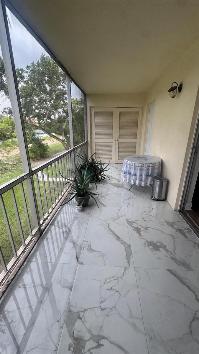 A screened-in balcony features white marble-look tile flooring, two potted plants, and a small table — 636 NW 13th St # 0230, Boca Raton FL 33486, BOCA RATON, FL