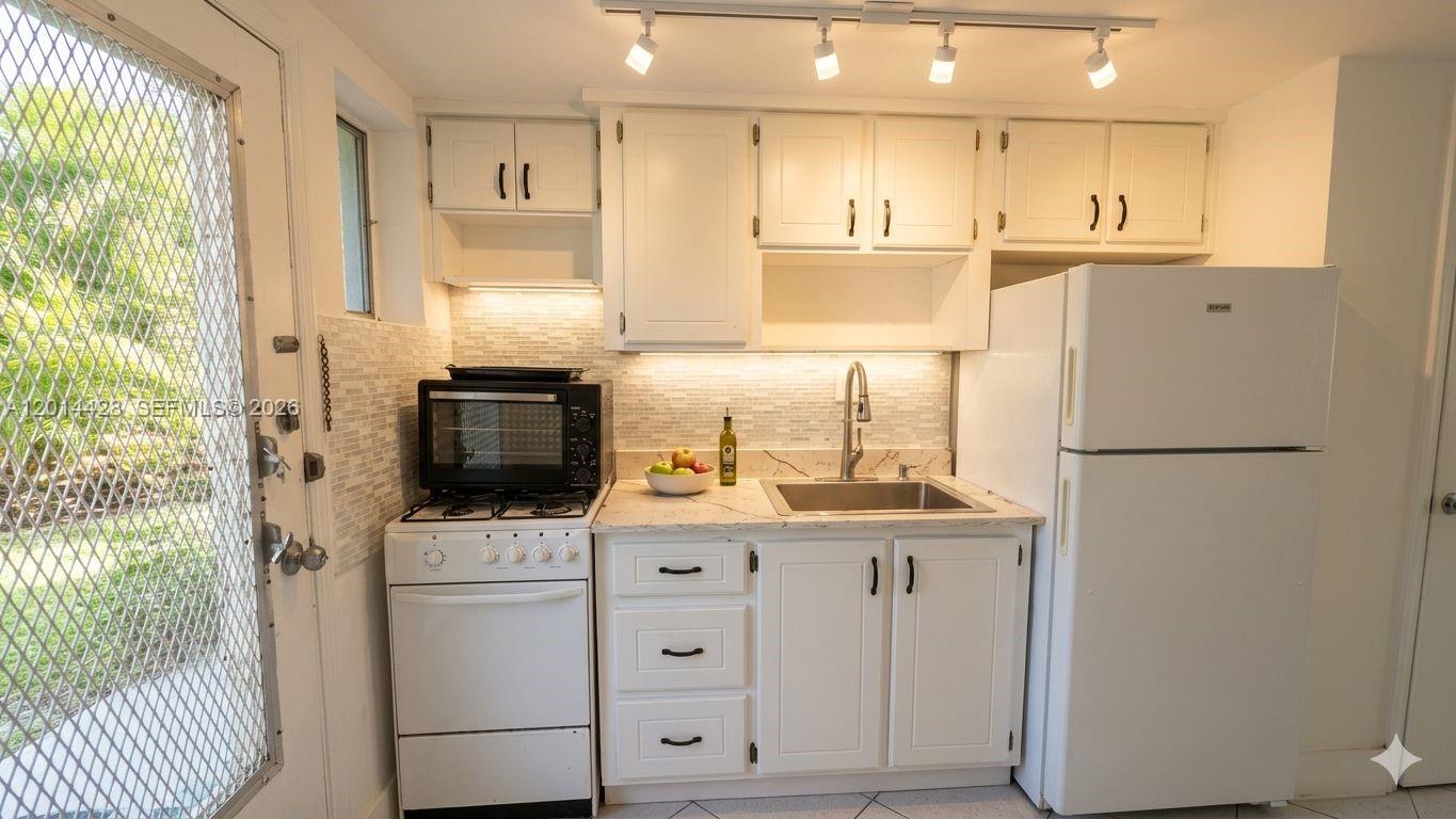 A small kitchen features white cabinets, a white stove, a refrigerator, and a tiled backsplash — 6490 Collins Ave # 14, Miami Beach FL 33141, MIAMI BEACH, FL