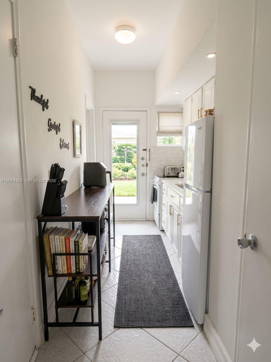 A narrow galley kitchen features white cabinets, a refrigerator, a console table, and a glass door — 6490 Collins Ave # 14, Miami Beach FL 33141, MIAMI BEACH, FL