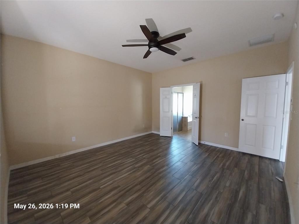 An empty bedroom features light-colored walls, wood-look flooring, a ceiling fan, and two doorways — 2228 PARROT FISH DRIVE, HOLIDAY, FL