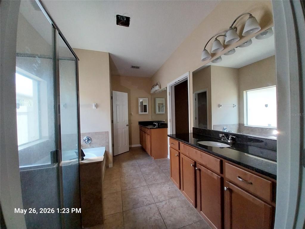 A bathroom features dual wood vanities with black countertops, a glass shower, and tile flooring — 2228 PARROT FISH DRIVE, HOLIDAY, FL