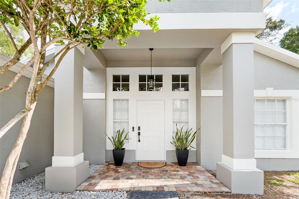 A white front door with sidelights and transom windows sits under a covered porch — 11225 FLOWER AVENUE, WEEKI WACHEE, FL